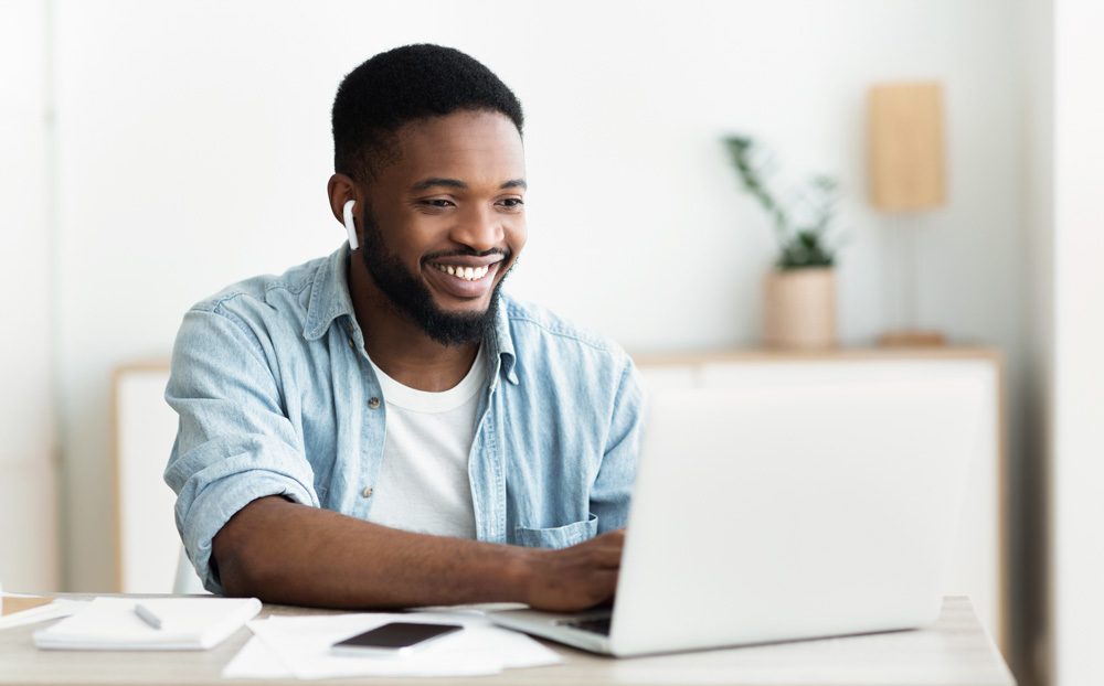 smiling man wearing earbuds typing on computer university of Dubuque online tuition and fees